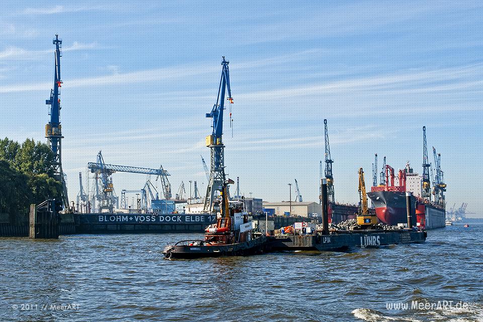 Ein Schlepper mit einem Arbeitsponton und einem Bagger vor den Docks von Blohm+Voss im Hamburger Hafen // Foto: MeerART