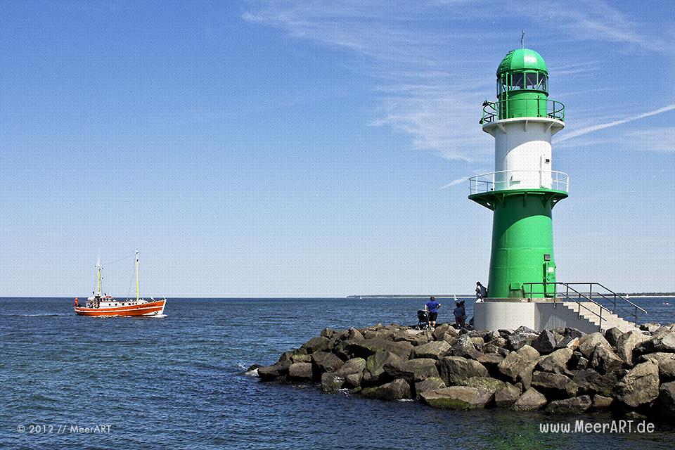 Ein Kutter läuft in den Hafen von Warnemünde ein, davor der grün-weiße Leuchtturm auf der Mole // Foto: MeerART